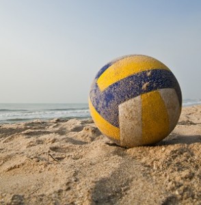 A beach volleyball sits on the sand with the ocean in the background