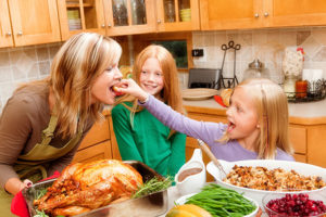 mother and two daughters with thanksgiving feast in kitchen with roasted turkey, green beans, stuffing, and cranberries