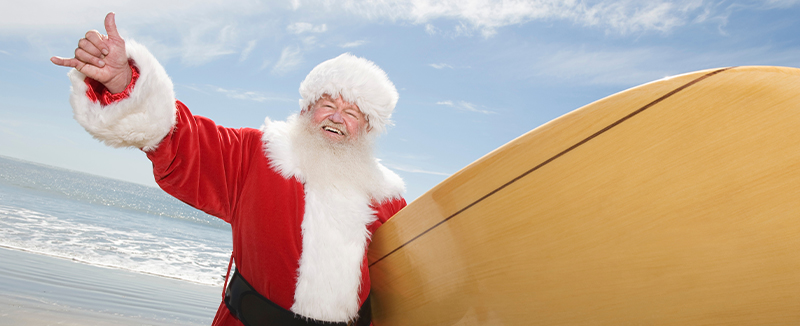 man dressed as Santa holding surfboard