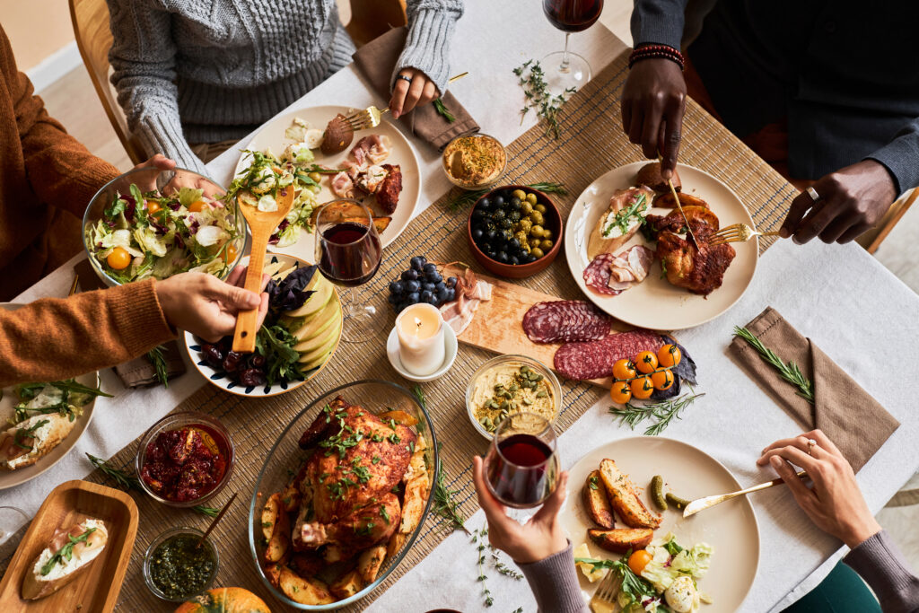 group of friends enjoying thanksgiving food at festive dinner table with roasted turkey